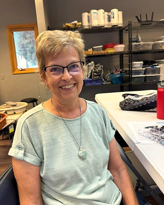 A smiling person in the studio wearing a wire-wrapped stone pendant