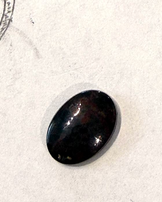 A dark, red-flecked cabochon stone resting on a sheet of sketch paper
