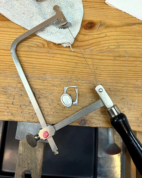 A jeweler’s saw and a small silver bezel on a wooden bench pin