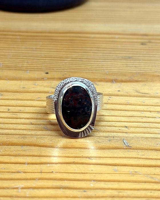 A finished silver ring with a bezel-set, red-flecked stone on a wooden bench